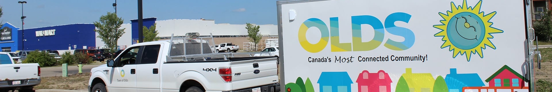 White pick up truck with the Town of Olds municipal logo with a colourful trailer hitched to the back, reading "Olds - Canada's most connected community!"