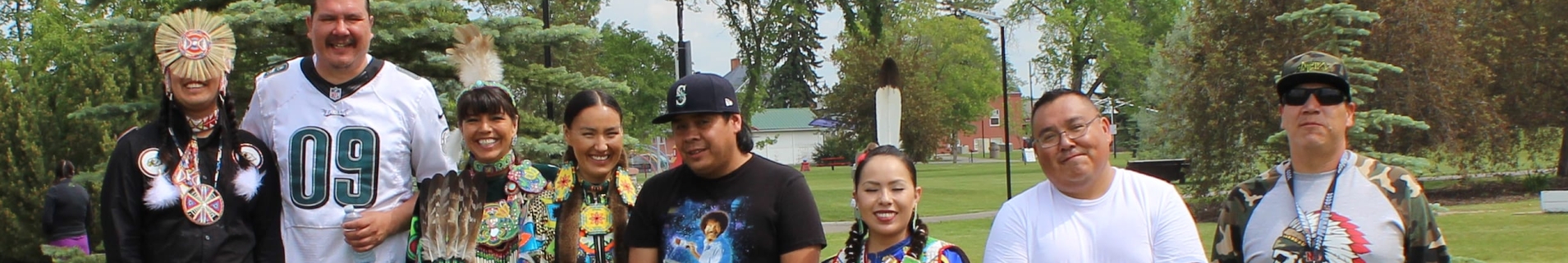Group of young adults standing in a line, some wearing traditional indigenous attire and smiling