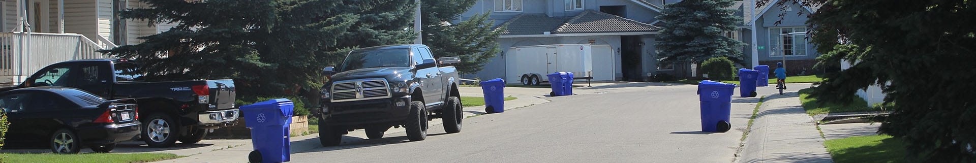 Residential street with a black pick-up truck parked and blue waste bins on the curb